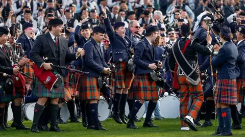 Getty Images Members of the Simon Fraser University pipe band celebrating their win. Some are shouting with joy and raising their hands in the air. They are wearing traditional piper outfits with hats, A woman in the middle is jumping in the air