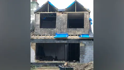 Nick Marns An extension to a two-storey house, which does not yet have any doors or windows. It is being held together by wooden beams.