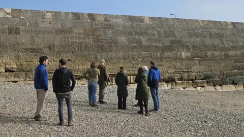 Dorset Council Officials on the gravel beach looking up at The Cobb.