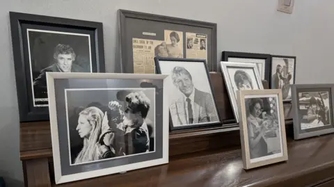 Photos of Shirley Bartlett doing make-up and others of celebrities and their autographs on a shelf. 