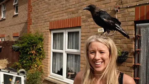 Crow sits on the head of a woman. The woman is smiling.