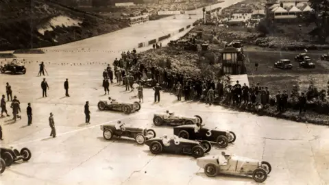 Brooklands Museum An old sepia photo of a motor race. 