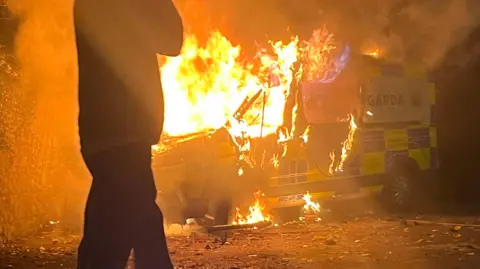 Getty Images A man in front of a police van which is on fire.