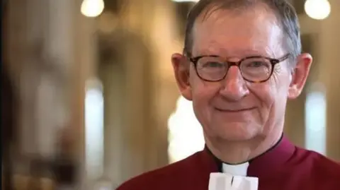 Paul Marriot Dean wearing his red cloak with a white tie- smiling for camera 