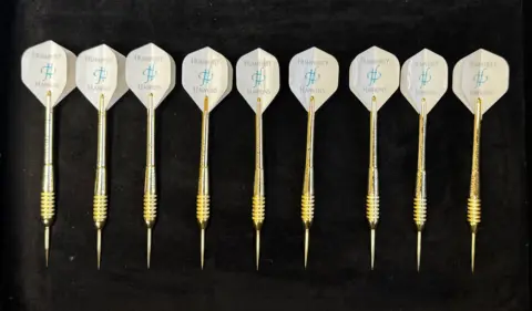 Nine golden darts laid down on a table in a row.