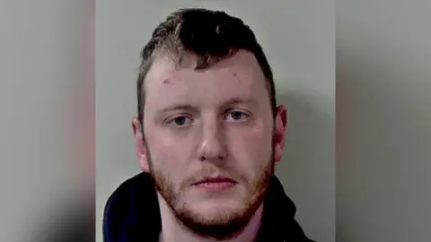 A mugshot of a man with short hair and a beard.