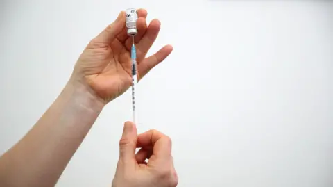 A pair of hands putting a needle in a vial.