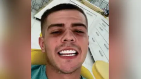 Coran Davies Coran Davies sitting in a yellow dentists chair. He is smiling at the camera, showing his teeth. He is wearing a green t-shirt