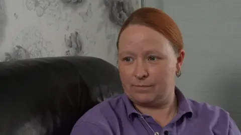 Qays Najm/BBC A head and shoulders shot of Victoria Pyett sitting on a black leather sofa. She is wearing a purple polo shirt and is looking to the left of the camera.