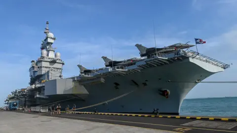 AFP via Getty Images The aircraft carrier pictured in 2025 while moored up in Singapore during a media tour, against a blue sky with partial cloud cover.
