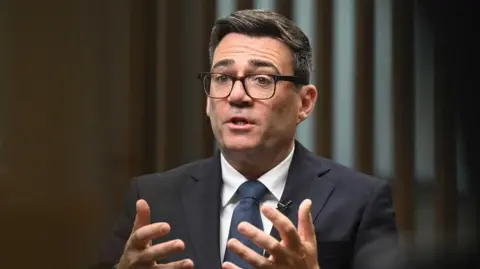 Andy Burnham seated during an interview, holding his hands in front of him while speaking 