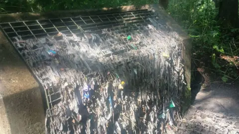 A large grate where the front is encrusted with detritus, including many wipes and cloths.