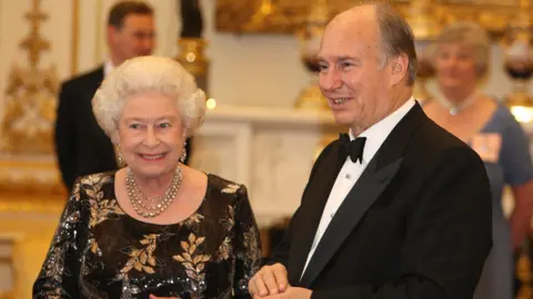 PA HAPPY Elizabeth II wearing black dress with gold sheet patterns by side by side khan wears a black tuxedo