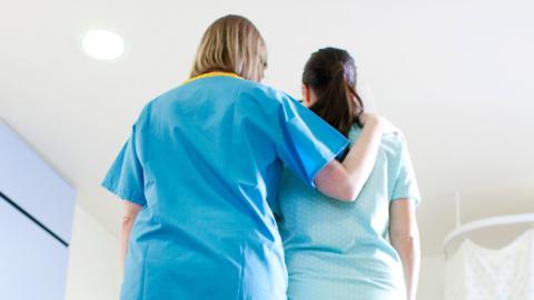 A nurse comforts a woman in a blue gown in a hospital room