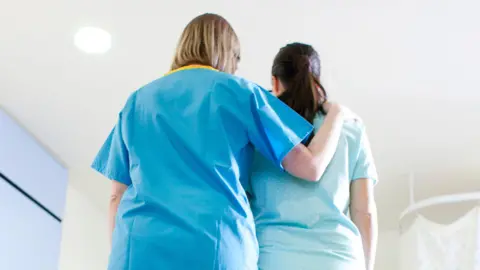 A nurse comforts a woman in a blue gown in a hospital room