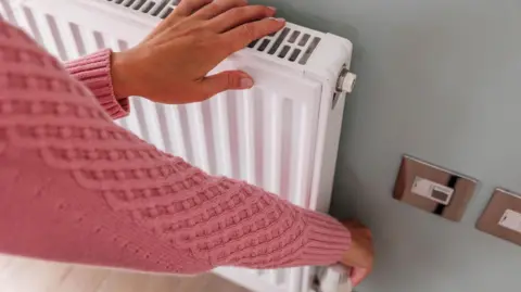 Getty Images Woman's hands adjusting a heating temperature on a radiator at home 