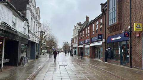 Image shows wet Havant high street, with shops and a lone person walking down the pedestian precinct 