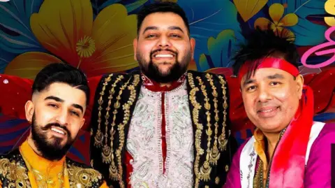 Black Country Multicultural Day Three people posing together in front of a colorful floral backdrop, wearing brightly colored embroidered traditional outfits. The person in the center wears a red and black garment with gold detailing, while the others wear yellow and magenta outfits with decorative embellishments.