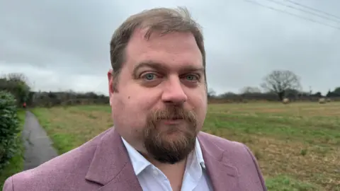 Dave Robertson, the Labour MP for Lichfield, in a mauve suit jacket standing in front of a field and a footpath