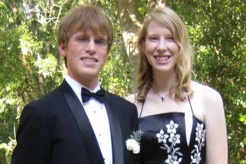 Kate Grosmaire Photo of Conor McBride, in a black tie and jacket and white shirt, and Ann Grosmaire, in a black dress with white flowers, smiling at the camera