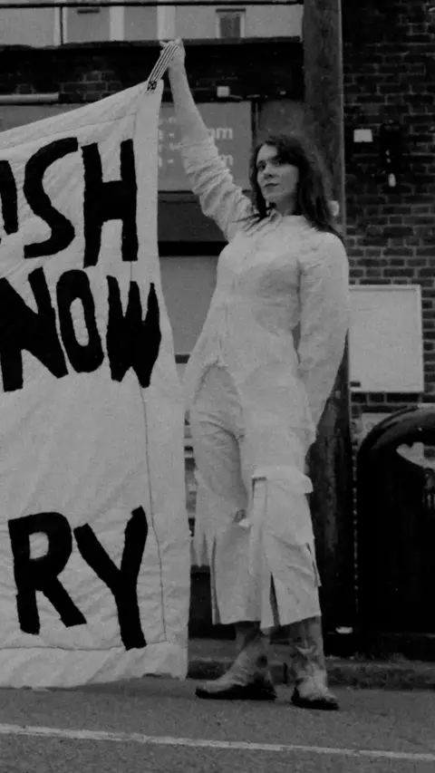 Kate Nash in white outfit holding banner up