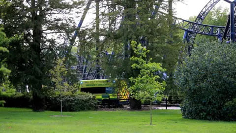 Getty Images An ambulance is parked at the base of a rollercoaster, with the twists and turns of the track seen behind a series of trees.