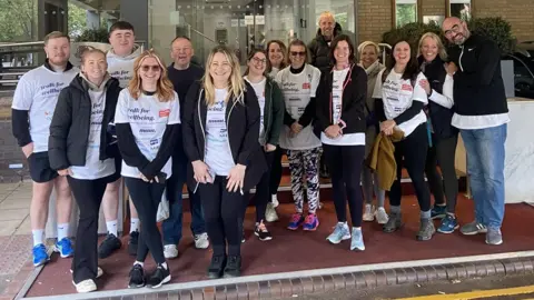 A group of hotel staff from businesses in Empica Bristol and Bath pose for the camera before heading out on a charity walk. Many wear white T-shirts with the charity's logo on them and they are mostly smiling