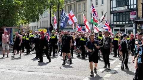 A group of protesters holding English, Welsh and British flags on a street in Bristol city centre along with police. 