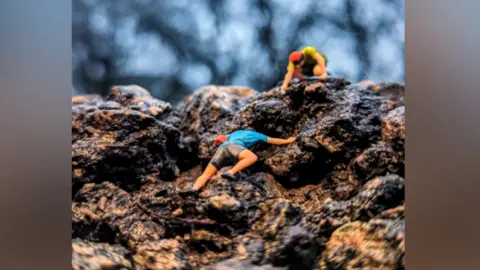 Dave Fargher Miniature mountain climber figures placed inside a pothole, pictured as though they are climbing a mountain