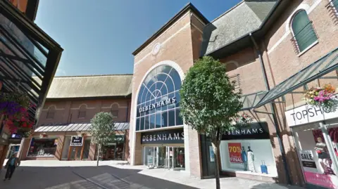 The Debenhams store is a multi-storey brick building. It has a grand arch window with a sign reading: "Debenhams" on it.