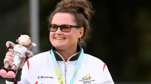 Getty Images Bowler Lucy Beere won a silver medal for Guernsey in Birmingham 2022. She is pictured wearing the medal, Team Guernsey kit and holding the Birmingham Games mascot toy, Perry the bull