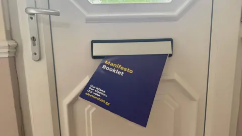 BBC A blue Manifesto booklet coming through the post box of a white door