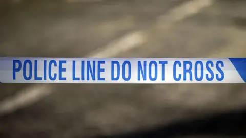 A blue and line police tape reading POLICE LINE DO NOT CROSS