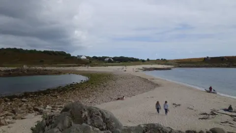 View across a sand bar at low tide, taken from St Agnes, with Gugh in the ditance - connected by sand with a few people walking and sun bathing.