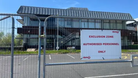 LDRS A car park at County Hall with a barrier around it and a closed sign that says "exclusion zone authorised personnel only". There is a large building with a metal-type roof in the background.