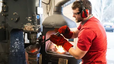 Lancaster Armoury An apprentice stood in the workshop, shaping a piece of red hot metal with a large press