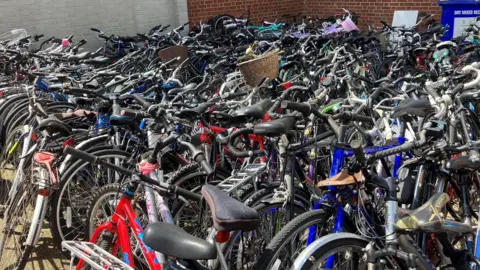 Chris Goreham/BBC A multitude of bikes lined up in rows. They have different coloured frames, while some have baskets on the front.
