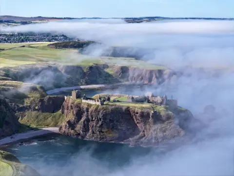 James Barrie A castle as fog drifts away from it, with the sea surrounding it