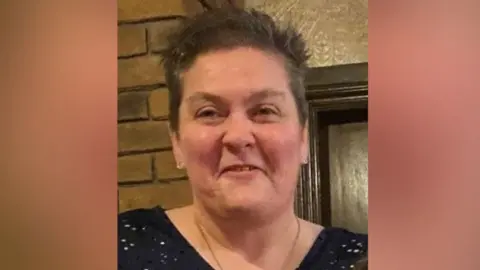 Ann Marshall is smiling at the camera. She has short brown hair and is wearing a black top.