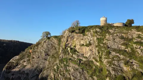 WeatherWatcher/Mrsbrispie A view across Avon Gorge showing the Clifton Observatory above a steep rocky cliff with a stunning blue sky behind.