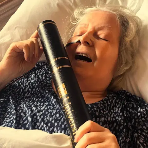 Janey Godley/X Janey Godley holding a black tube with the University of Glasgow logo on it