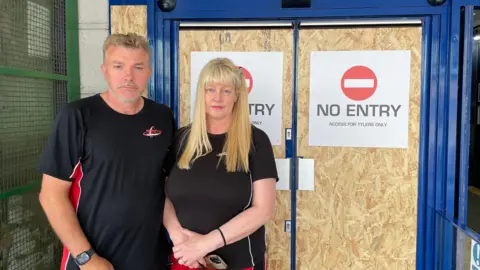 Sean and Julie Hutton stand before doors with boards on