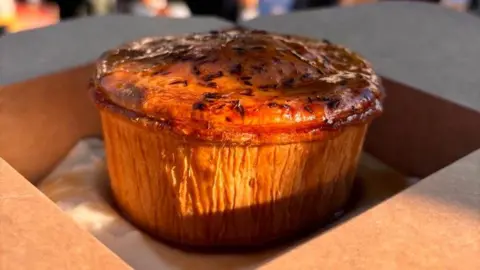 Tommy Banks Pie and mash, covered with gravy, in a cardboard takeaway box