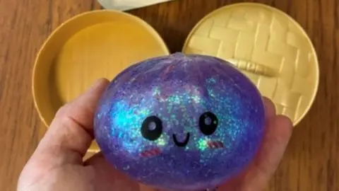 Hull City Council One of the squeezy dumpling toys being held. It is made of sparkly purple plastic and has a plastic steamer 