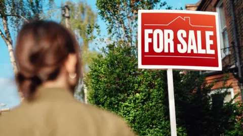 Getty Images Image of a woman looking at a For Sale sign outside a house