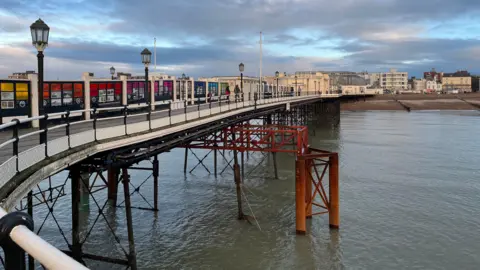 George Carden/BBC A red steel metal truss which is supporting the pier. It has three legs on either side which go into the ocean