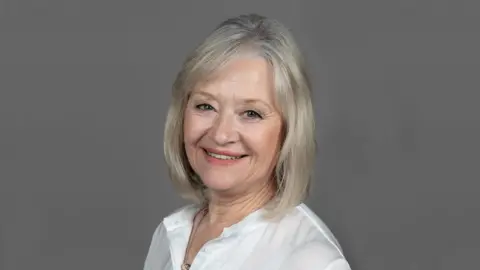 University Hospitals Birmingham NHS Foundation Trust A head shot of Dame Yve Buckland who is wearing a white shirt with a grey background