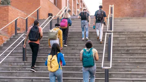 Group of diverse university students walking up outdoor steps, carrying backpacks and heading to classes.