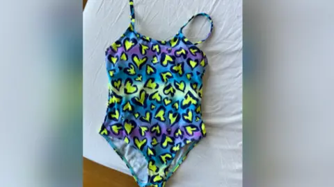 Kayleigh Shore Multi-colour swimsuit with neon yellow and black leopard print hearts on a blue base colour. The swimming costume is laid flat.