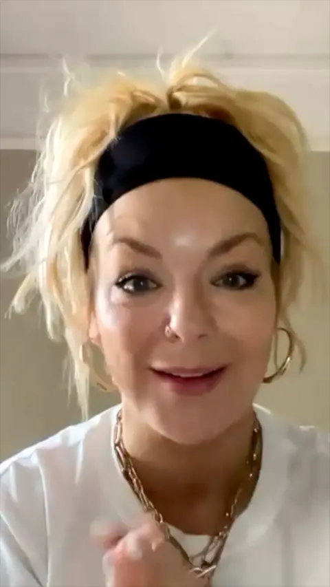 Sheridan Smith smiling. She has blonde hair tied up and is wearing large hoop earrings.
